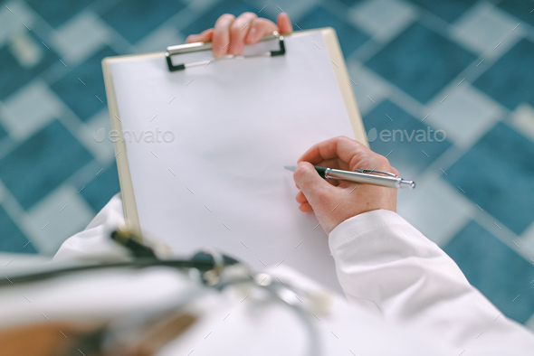 Female doctor in white uniform writing on clipboard paper - Stock Photo - Images