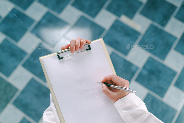 Female doctor in white uniform writing on clipboard paper - Stock Photo - Images