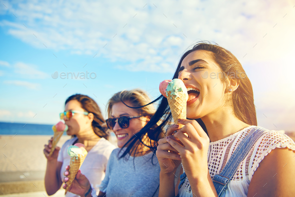 Three young woman eating ice cream at the seaside - Stock Photo - Images