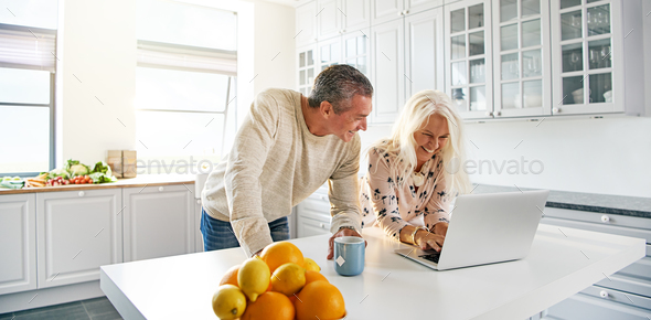 Senior couple relaxing in a kitchen with a laptop - Stock Photo - Images