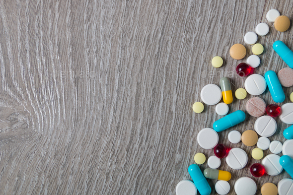 lot of colorful medication and pills from above on grey wooden background.  Copy space. drugs. Stock Photo by bondarillia