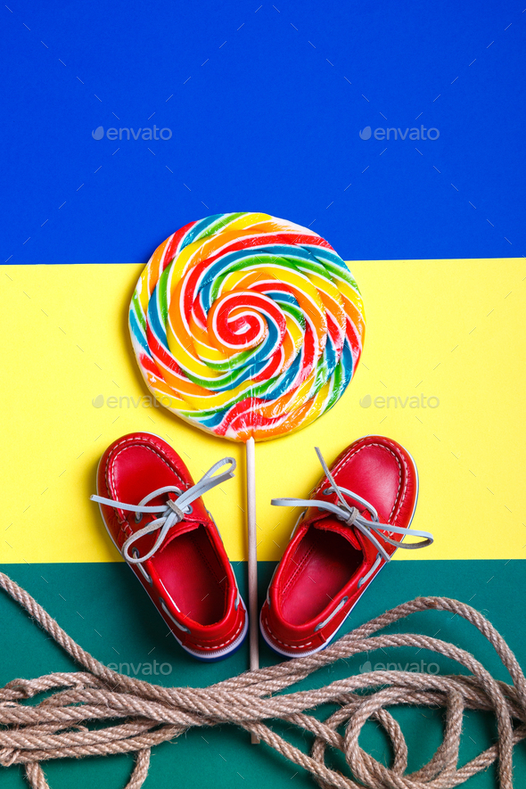 Small red boat shoes near big multi-colored lollipop