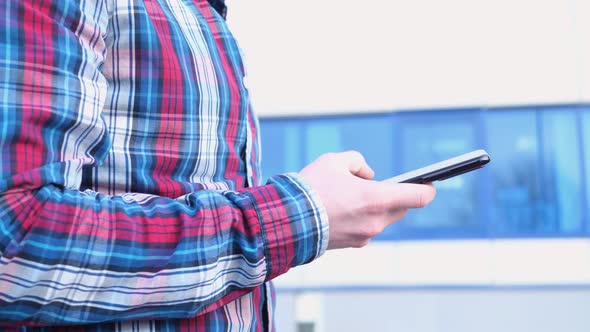 A man's hand in a checkered red-blue shirt holds a smartphone.