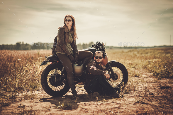 Stylish cafe racer couple on the vintage custom motorcycles in a field