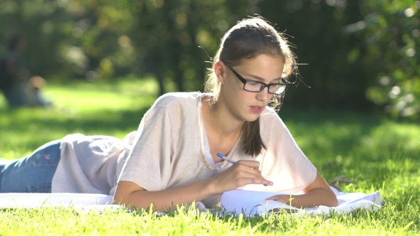 Young Beautiful Girl On Meadow Writes To Notebook