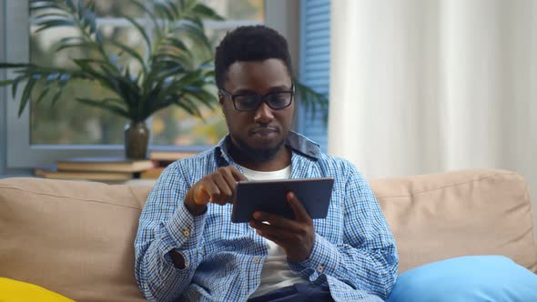 Portrait of Satisfied Afro Guy Using Digital Tablet Sitting on Sofa at Home alt