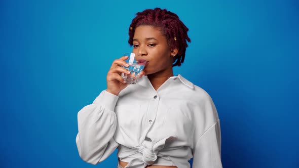 Beautiful Healthy Afro Woman Drinking Water From a Glass Against Blue Background