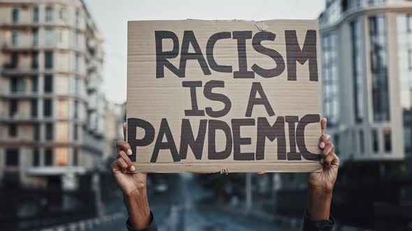 Hands of Unknown Africanamerican Person are Raising Up Cardboard Poster Racism is a Pandemic Posing alt