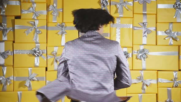A Cheerful Young Man in an Elegant Gray Suit is Dancing in a Room Full of Gift Boxes Posing for the alt