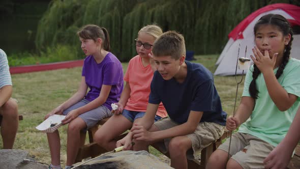 Kids at summer camp roasting marshmallows around campfire