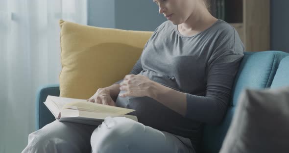 Pregnant woman reading a book and relaxing on the sofa