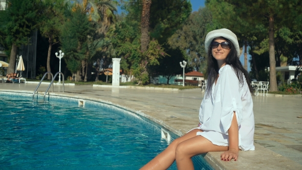 Slender Young Woman In a Hat Sits On The Edge Of The Swimming Pool, Sexy Long Legs. alt