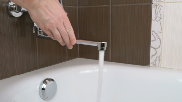 Water Stream Flows From The Water Tap Into The Tub