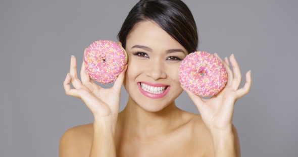 Laughing Woman Holding Two Pink Donuts To Her Eyes alt
