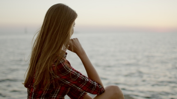 View Of a Young Girl Sitting Down By Sea Shore Looking At The Horizon
