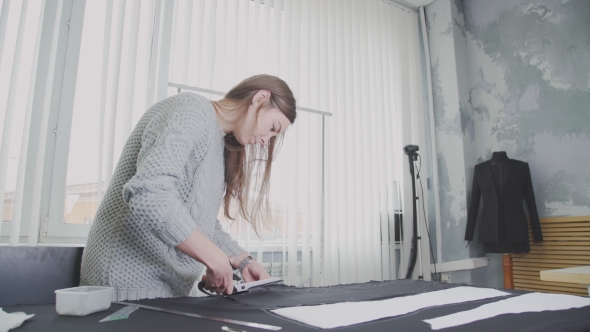 Young Woman In a Little Design Studio Cutting Fabric Using a Scissors
