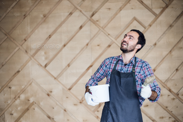 Man with tin of paint and brush looking up on a wooden wall background. Copy space for your text