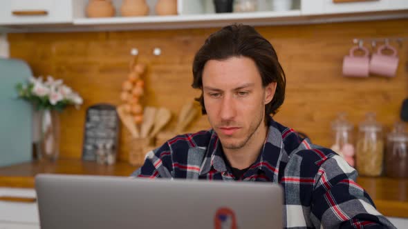 Portrait View: A Young Man Working From Home at the Notebook in Kitchen Room.