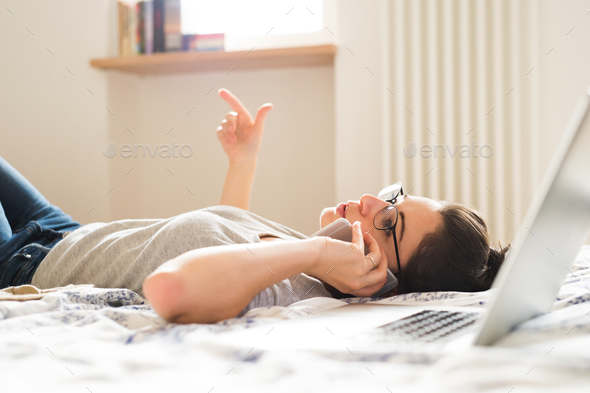 Woman lying on bed, working on laptop, calling. Home office. - Stock Photo - Images