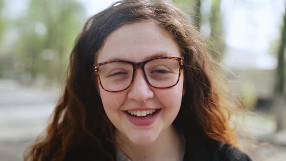 Portrait of a Redhaired Girl in Glasses Looking at the Camera and Smiling alt