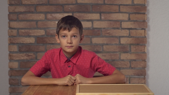 Child Sitting at the Desk Holding Flipchart with Lettering Ok on the Background Red Brick Wall. alt