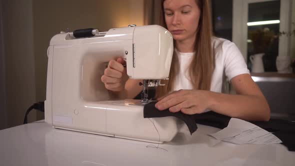 Woman Sews a Black Protective Mask on a Sewing Machine. Cuts Black Threads with Scissors.