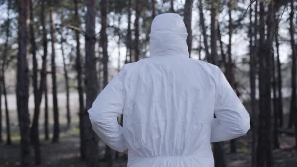 Back View of Young Caucasian Man in White Safety Suit, Protective Eyeglasses and Face Mask Running alt