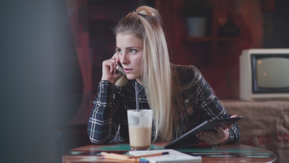 Young and Beautiful Girl in a Cafe Drinking Coffee and Talking on a Cell Phone.