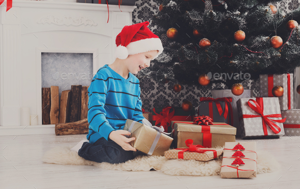 Cute boy in santa hat unwrapping christmas presents - Stock Photo - Images
