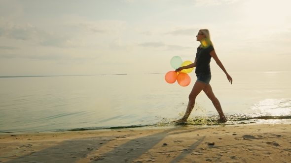 Carefree Young Woman Walks Along the Beach in the Beautiful Sky, Is Holding Balloons alt