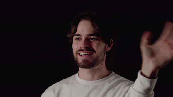 Trendy Young Man waving into camera, welcoming gesture, close, black background alt