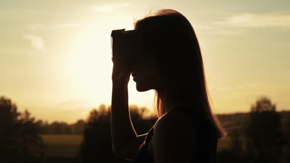 Woman Uses a Virtual Reality Glasses in the Forest at Sunset