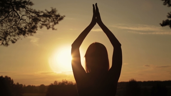 Happy Young Woman Silhouette Against Sky Lifts Hands Up in Air