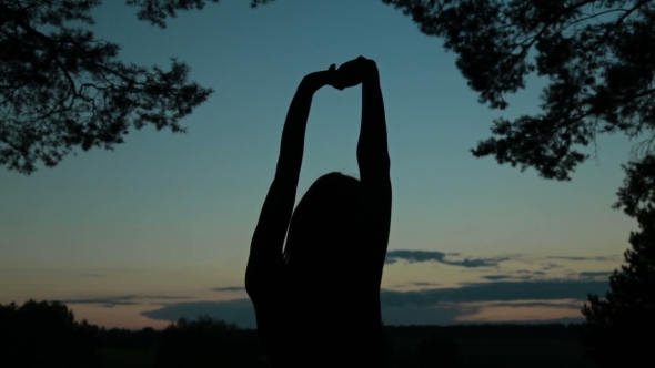 Young Woman Stretching Towards the Sky in the Forest After Sunset