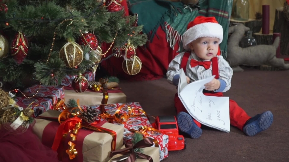 Child Sitting Under the Tree and Leafs Through a Notebook alt