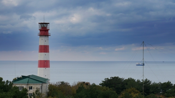Cargo Ship Passes By a Beautiful Majestic Lighthouse Under Dramatic Stormy Clouds