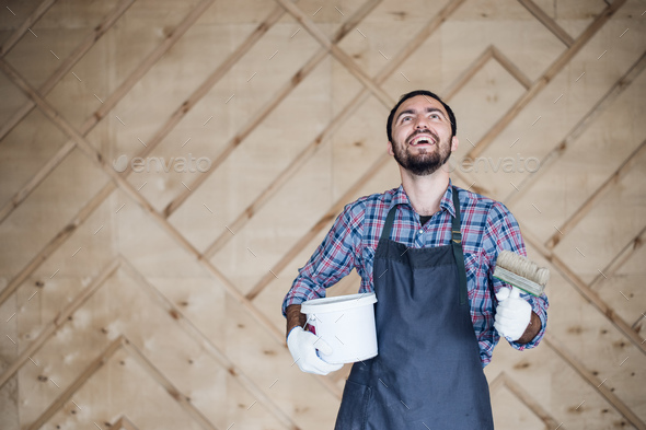 Man with tin of paint and brush looking up on a wooden wall background