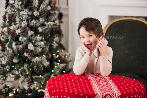 boy calls Santa while sitting on a big green armchair at home over chirstmas tree background
