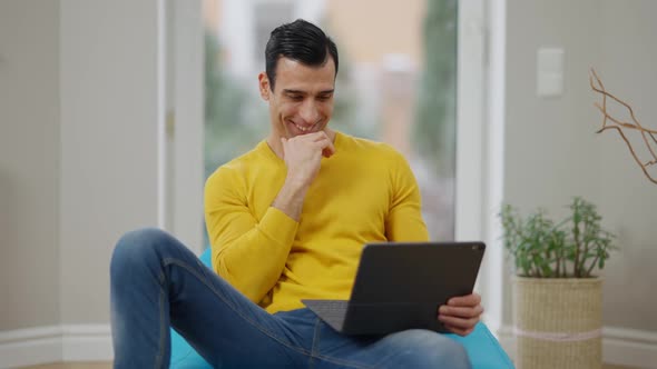 Relaxed Cheerful Middle Eastern Man Laughing Watching Movie on Tablet at Home alt