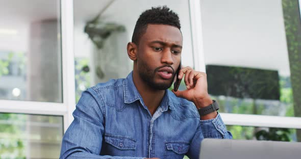 African american businessman talking on smartphone and using laptop outisde cafe cmmunication, busin alt