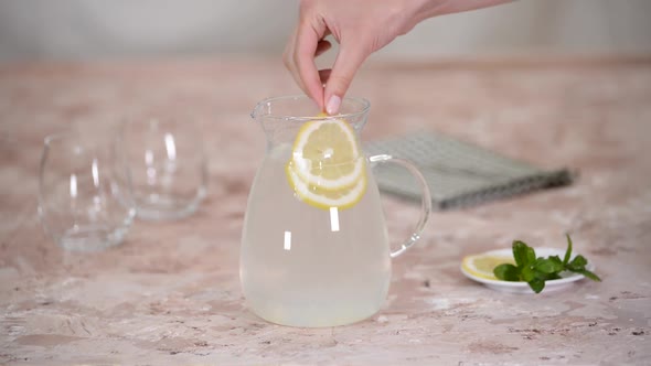 Female Hand Puts a Slice Lemon Ana Mint in Jug for Lemonade
