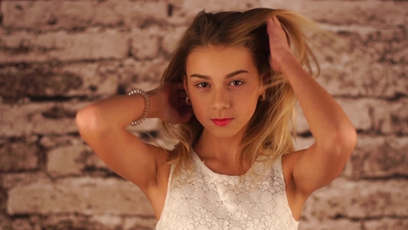 Young Teenage Girl Is Staying Near the Wall, Playing with Hair,looking at the Camera and Smiling