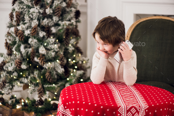 boy calls Santa while sitting on a big green armchair at home over chirstmas tree background