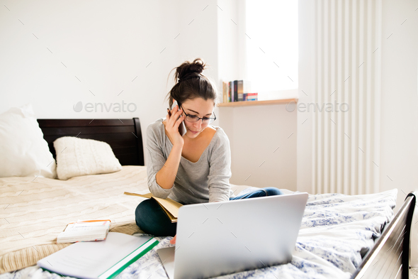 Woman sitting on bed, working on laptop, calling. Home office. Stock Photo  by halfpoint
