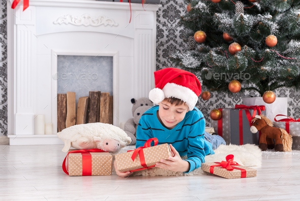 Cute boy in santa hat unwrapping christmas presents - Stock Photo - Images