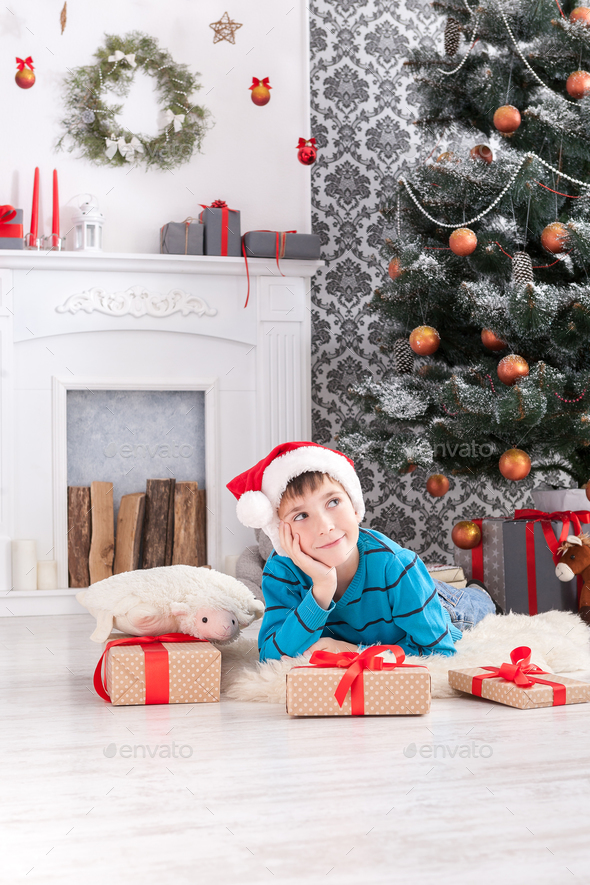 Cute boy in santa hat unwrapping christmas presents - Stock Photo - Images