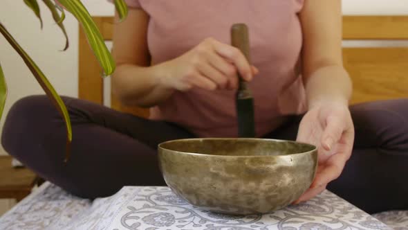 Woman in cozy outfit and lotus pose playing Tibetan singing bowl in her meditation,close up.