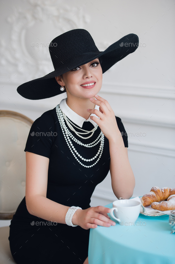 Woman in hat, much like the famous actress, croissant eating and drinking tea.