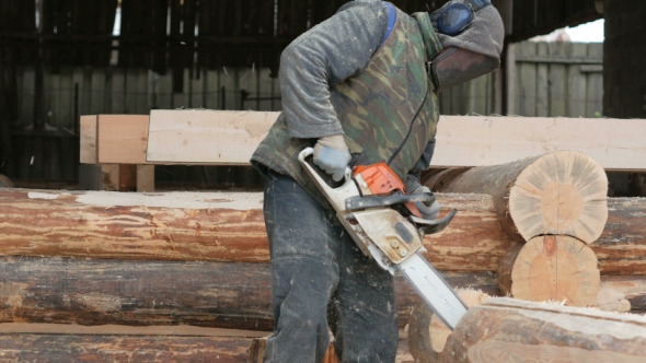 Construction Worker Cuts Wood Chainsaw for Future Home. Protective Mask and Headphones on the Head