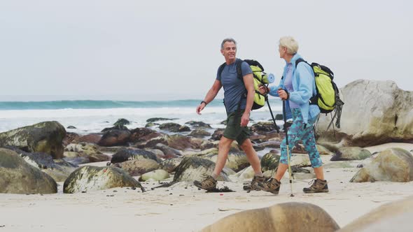 Senior hiker couple with backpack and hiking poles talking to each other and walking while hiking alt